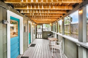 A covered outdoor area with wooden flooring, white chairs, and a blue door. - Mermaid Beach Cottage Prime Vilano Beach Dogs OK (St. Augustine)