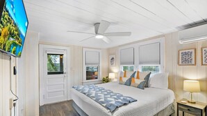 Un dormitorio con cama, ventilador de techo, televisor y ventana con persianas.