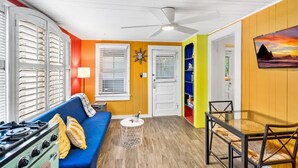 Un espacio habitable pequeño con un sofá azul, una mesa de comedor con sillas, una mesita redonda y una estufa.