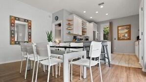 Eine moderne Küche mit weißen Schränken, ein Essbereich mit weißen Stühlen und ein Holzboden.