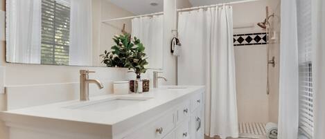 A bathroom with a white vanity, a large mirror, and a shower area.
