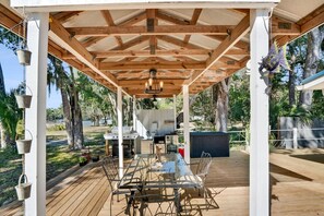 A covered outdoor dining area with a wooden deck, a glass table, and metal chairs. - On the Canal New Dock Kayak Bikes Beach Gear (Palm Coast)