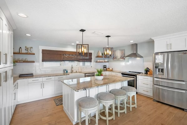 A spacious kitchen with white cabinetry, a large island with bar stools, stainless steel appliances, and pendant lighting.