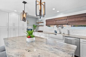 A modern kitchen with white cabinets, a granite countertop, and pendant lighting.