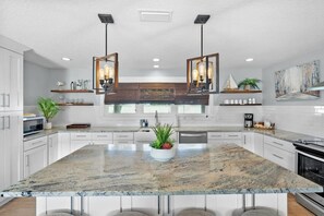 Een moderne keuken met een groot eiland, hanglampen en een plantenbak in het midden.