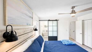 Een slaapkamer met een bed, een plafondventilator, een wandlamp en een schuifdeur naar een badkamer.