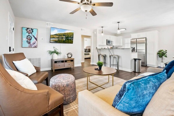 A modern living room with a brown leather sofa, a round coffee table, and a beige sofa with blue pillows. A ceiling fan is visible above the living area. - Water View Hot Tub Games Fire Pit Boat Parking (St. Augustine)