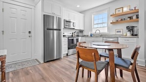 A modern kitchen with white cabinetry, stainless steel appliances, and a round dining table with wooden chairs. - Free Parking Big Patio Next to Restaurants Bars (St. Augustine)