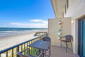 A balcony with a view of the beach, a table, two chairs, and decorative wall lights.
