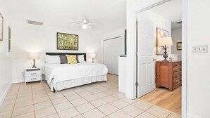 A bedroom with a bed, nightstands, a ceiling fan, a door leading to a bathroom, and a wooden dresser. - Just North of Historic St Aug Patio Garage BBQ (St. Augustine)