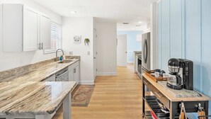 A modern kitchen with white cabinets, a marble countertop, and a coffee maker on a wooden table. - Just North of Historic St Aug Patio Garage BBQ (St. Augustine)
