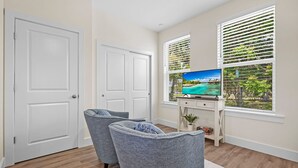A living room with a TV, two grey armchairs, a small table, and a window with blinds. - Downtown St Augustine Apt Smart TV Pack N Play (St. Augustine)