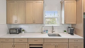 A modern kitchen with light wood cabinets, a built-in toaster, a sink, and a window with blinds. - Downtown St Augustine Apt Smart TV Pack N Play (St. Augustine)