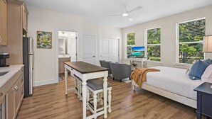 A modern kitchen with wooden cabinets, a dining table with chairs, a bed with a view of the outdoors, and a ceiling fan. - Downtown St Augustine Apt Smart TV Pack N Play (St. Augustine)