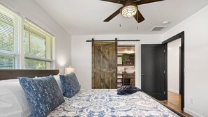 A bedroom with a large bed, a ceiling fan, and a sliding barn-style door leading to a bathroom. - Beautiful Kitchen BBQ Outdoor Dining Big Yard (St. Augustine)