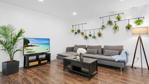 A modern living room with a flat-screen TV, a grey sofa, a coffee table, and a potted plant. - Beautiful Kitchen BBQ Outdoor Dining Big Yard (St. Augustine)