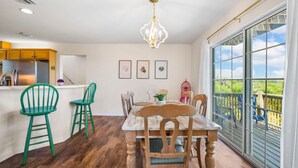 A dining area with a wooden table and chairs, a chandelier, and a view of a balcony with outdoor furniture.