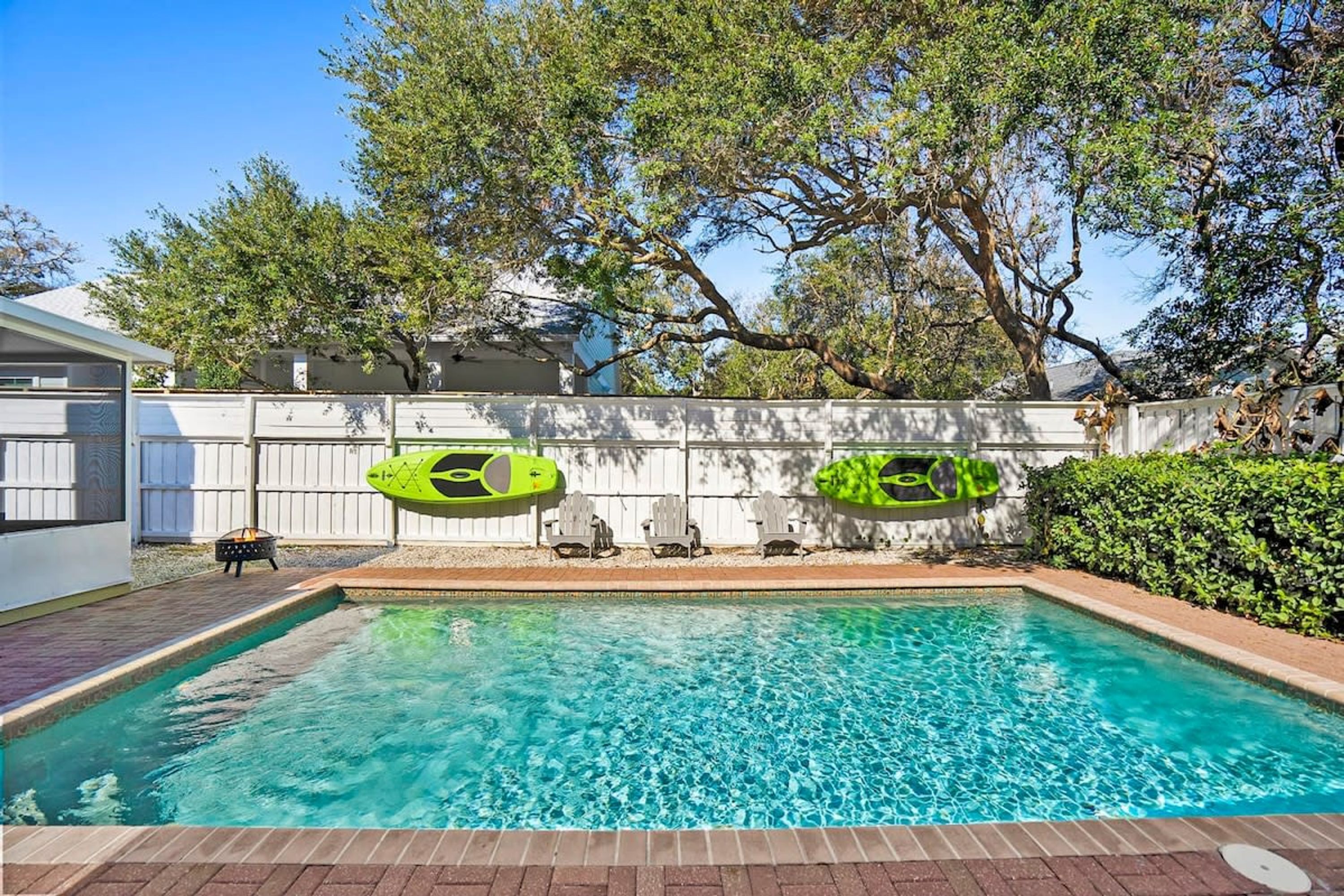 A rectangular swimming pool with clear blue water, surrounded by a brick deck. There are two green floating loungers attached to the poolside.