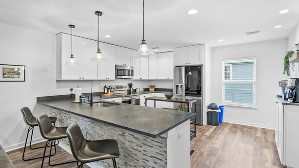 A modern kitchen with white cabinets, a central island with bar stools, stainless steel appliances, and pendant lighting. - Pool Spa Downtown by Beach FOY Add Golf Cart (St. Augustine)