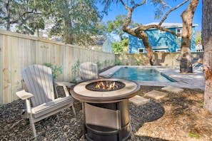 A backyard with a fire pit, two Adirondack chairs, a swimming pool, and a wooden fence.