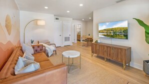 Ein modernes Wohnzimmer mit einer Couch, einem Couchtisch, einem an der Wand montierten Fernseher und einem Holzkasten.