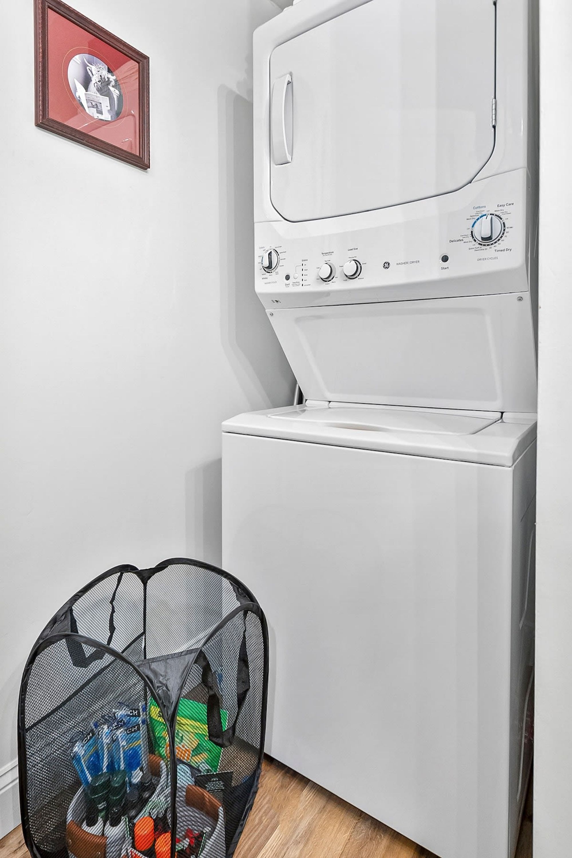Un espace buanderie comprenant un lave-linge et un sèche-linge, un petit espace de rangement fermé contenant divers objets, et un tableau encadré accroché au mur.