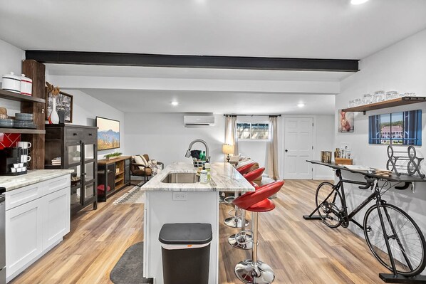 A modern kitchen with a central island, bar stools, a bicycle, and a dining area with a view. - Renovated Bungalow With Work Space Kitchen Patio (St. Augustine)