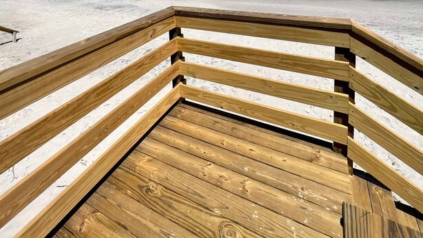 Eine Holzterrasse führt zu einem Strand, der von einem wolkenlosen, blauen Himmel überdacht wird.