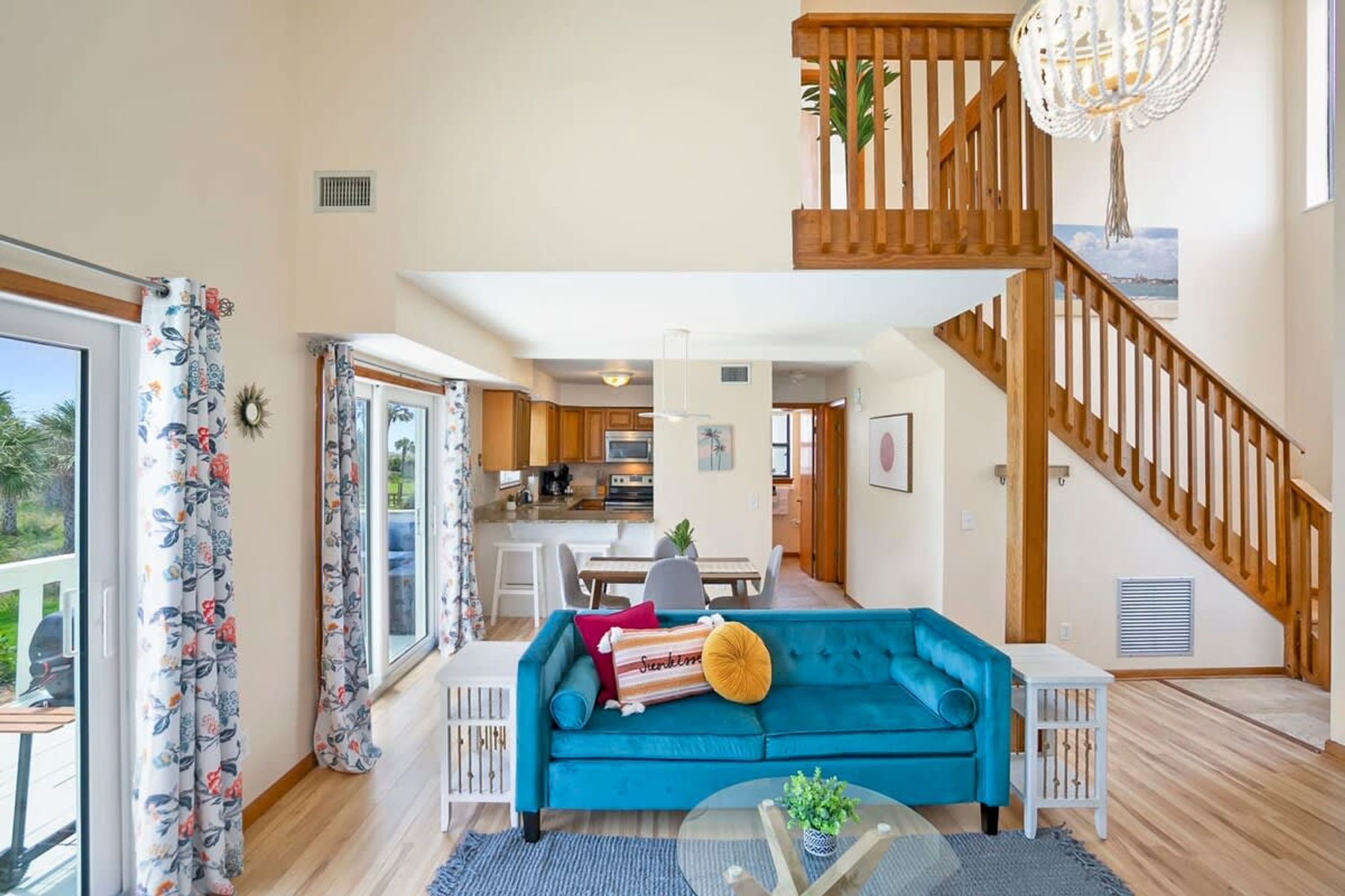 A spacious living area with a blue sofa, wooden staircase, and a view of the kitchen.