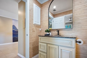 A modern bathroom with a wooden wall, a large mirror, a sink with a granite countertop, and a cabinet with drawers.