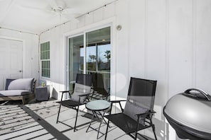 A sunlit patio with a grill, a sofa, and two chairs.