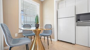 Uma cozinha compacta com forno embutido, geladeira e área de jantar com mesa de vidro e duas cadeiras.