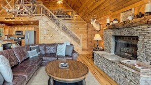 A wooden cabin interior with a stone fireplace, leather sofa, and a staircase leading to an upper level. - Hot Tub 3 Fireplaces Mountain Views Game Room (Blue Ridge)