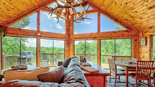 A spacious cabin with a large wooden ceiling, a leather sofa, a dining table, and a view of the outdoors. - Hot Tub 3 Fireplaces Mountain Views Game Room (Blue Ridge)