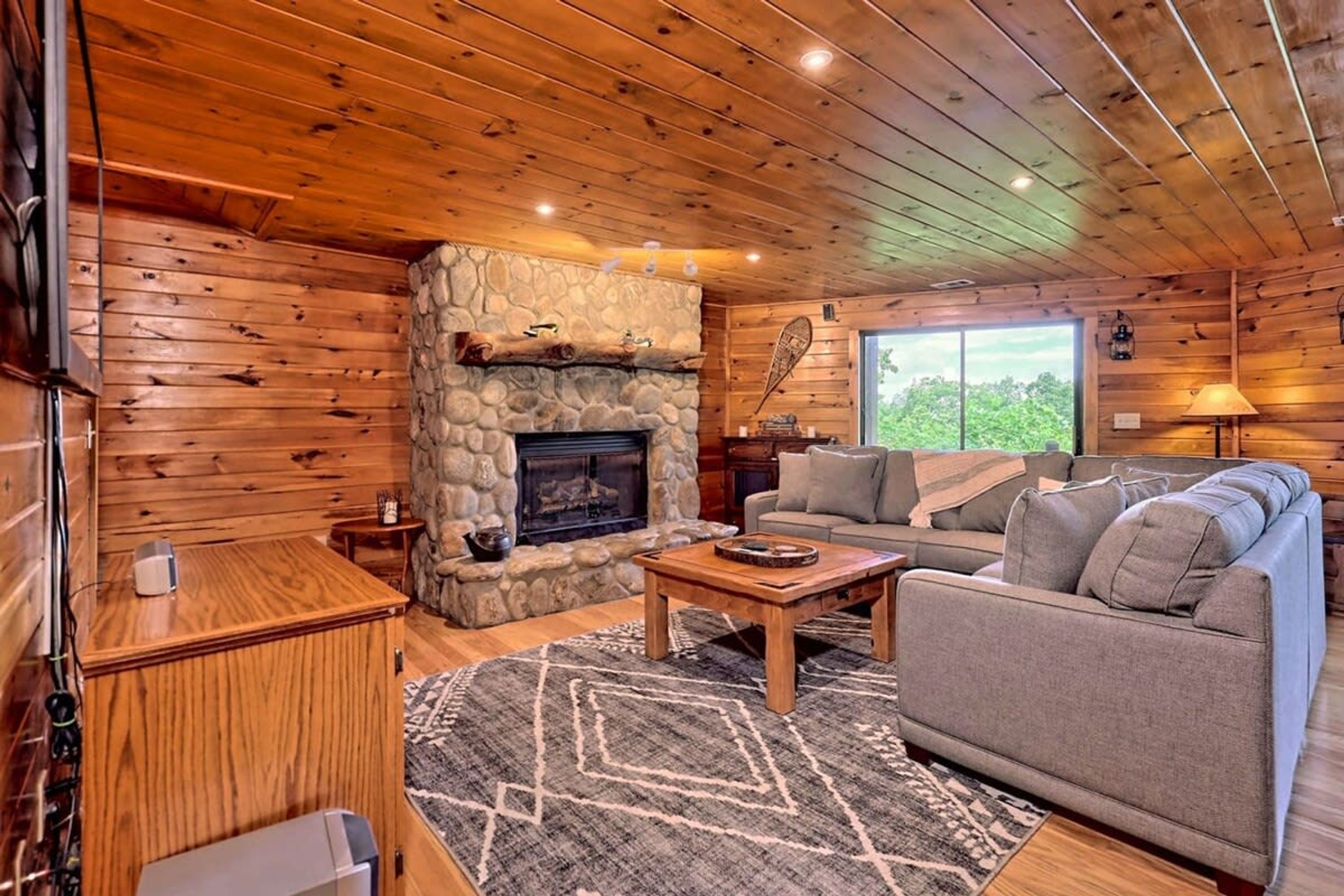 A cozy cabin interior with a stone fireplace, wooden walls, a sofa, and a coffee table.
