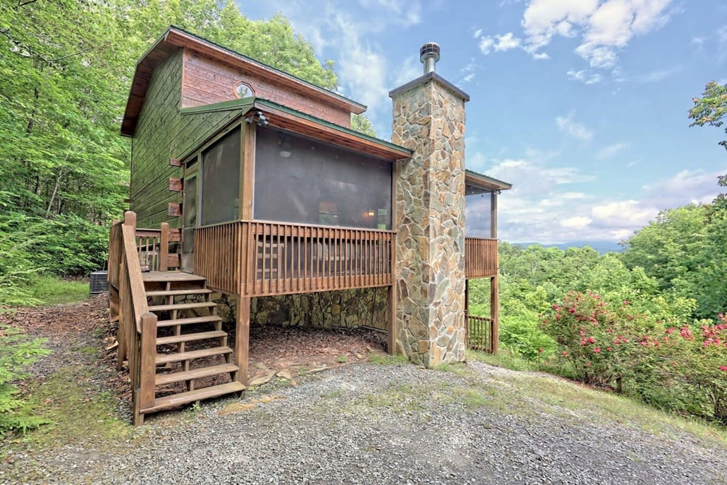 A cabin with a stone chimney, wooden deck, and a staircase leading to a windowed porch.