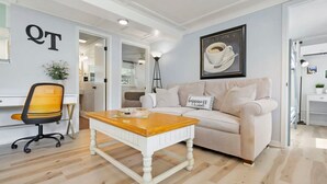 A modern living room with a white sofa, a wooden coffee table, and a framed coffee cup artwork on the wall. - Qt Cottage on Dunn s Creek Fire Pit Kayaks (Satsuma)