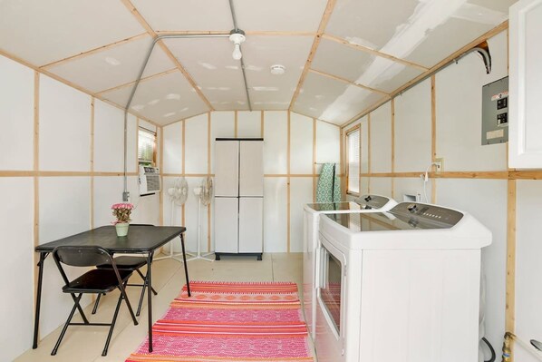 A compact kitchen with a white refrigerator, a white stove, and a small sink. There is a black chair and a table with a colorful rug. - Qt Cottage on Dunn s Creek Fire Pit Kayaks (Satsuma)