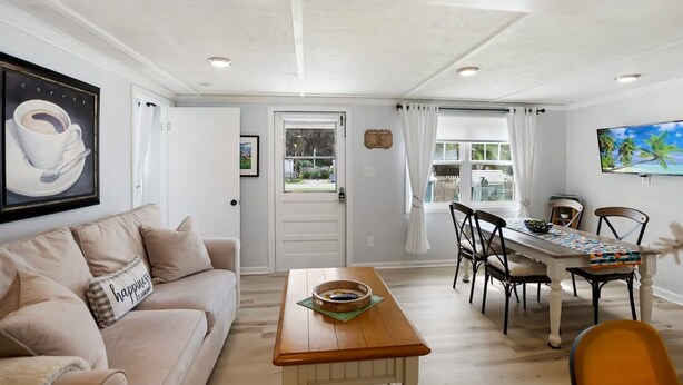 A living room with a sofa, a wooden coffee table, a dining table with chairs, and a painting on the wall. - Qt Cottage on Dunn s Creek Fire Pit Kayaks (Satsuma)