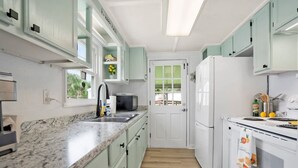 A kitchen with light green cabinets, a white refrigerator, a microwave, and a granite countertop. - Qt Cottage on Dunn s Creek Fire Pit Kayaks (Satsuma)