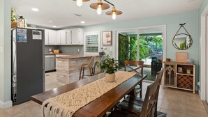 A modern kitchen with white cabinets, a built-in island, and a dining area with a wooden table and chairs. - Welcome Basket Pool By Beach Fire Pit BBQ PS4 (St. Augustine)