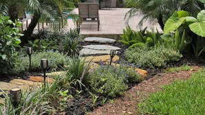A garden patio with a bench, a table, and an umbrella. - Welcome Basket Pool By Beach Fire Pit BBQ PS4 (St. Augustine)
