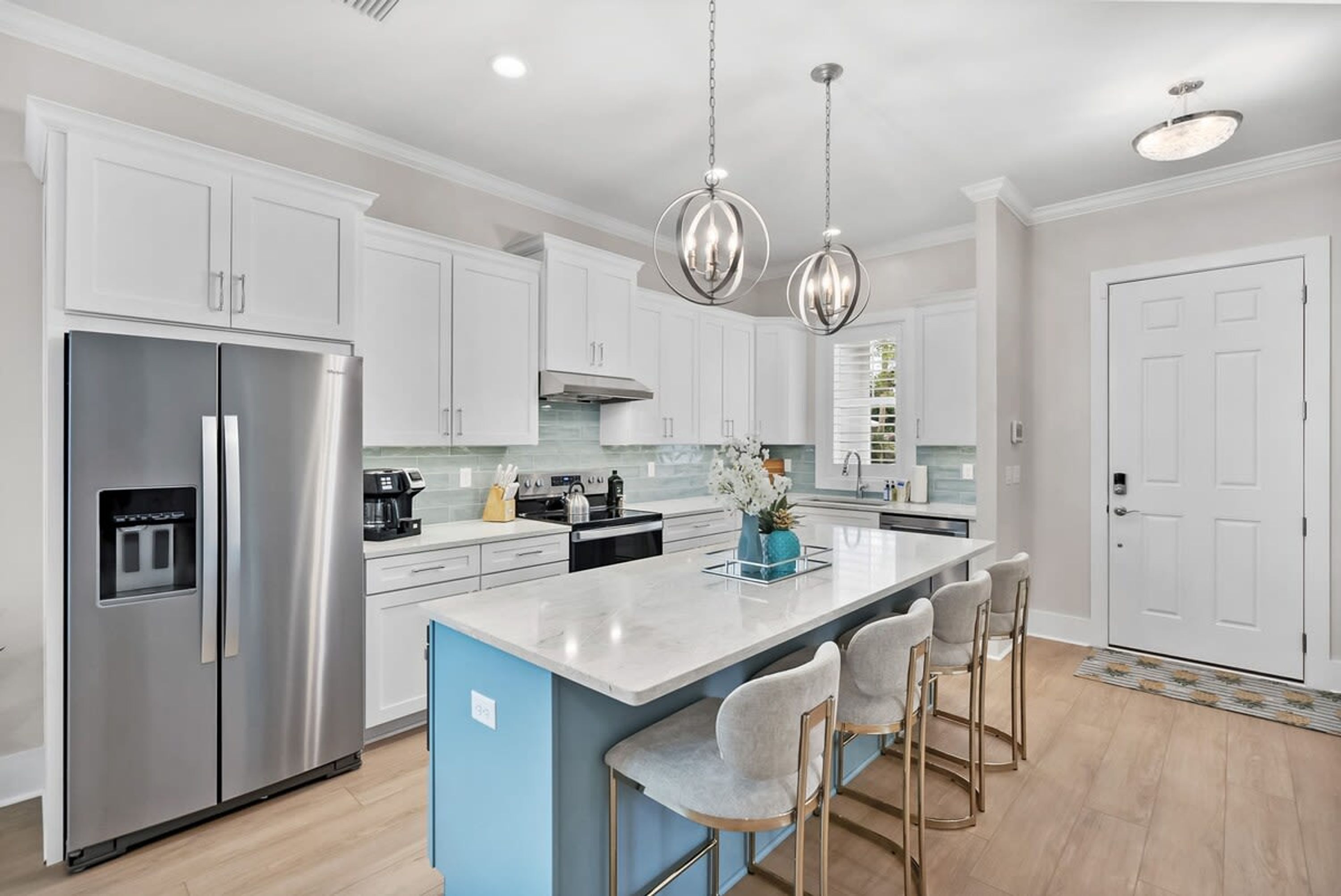 A modern kitchen with white cabinets, stainless steel appliances, a central island with bar stools, and pendant lighting.