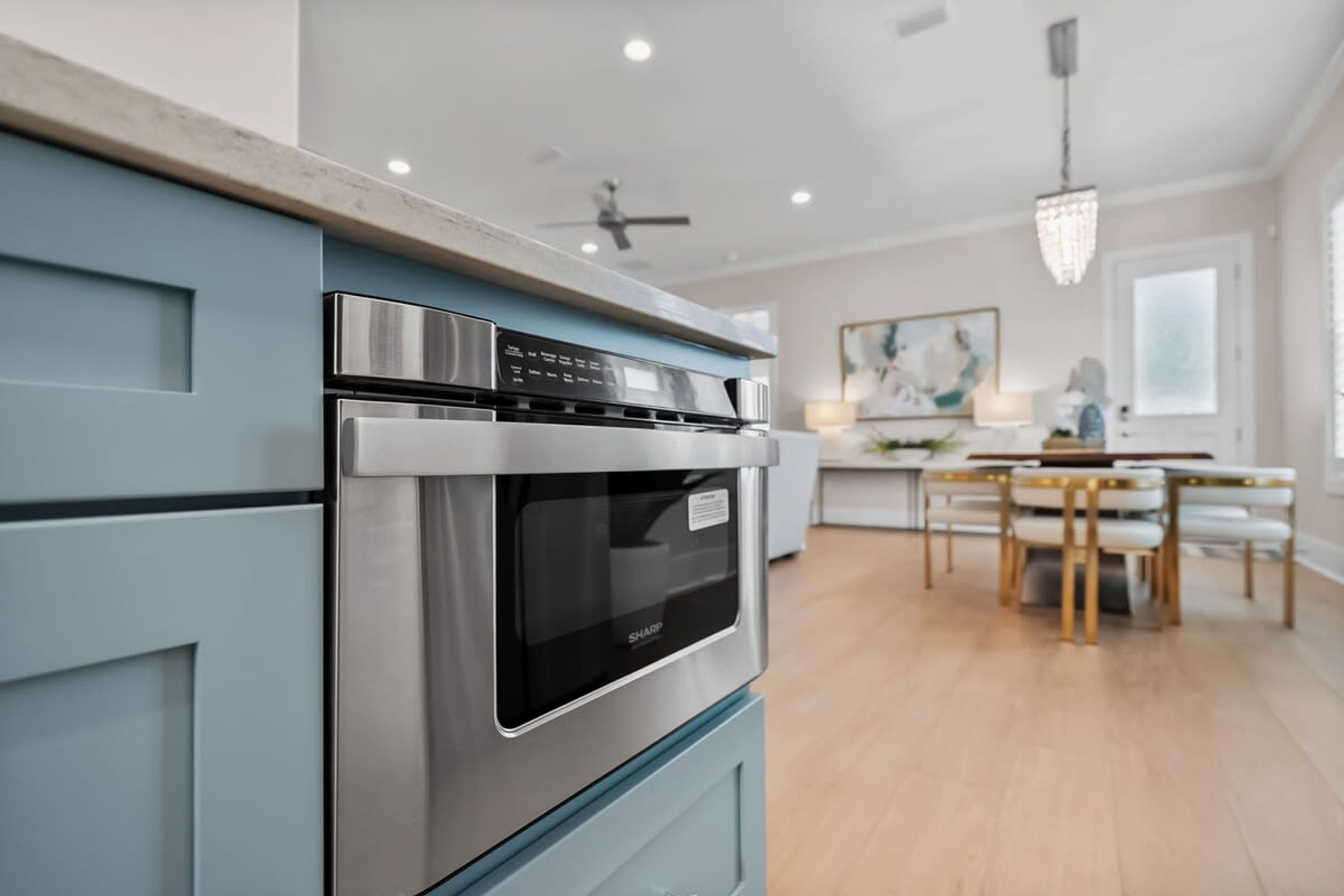 A modern kitchen with a built-in oven and microwave, a dining area with a table and chairs, and a chandelier.