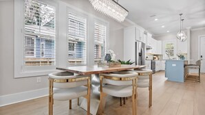Eine moderne Küche mit weißen Schränken, einem Holzespeisetisch und vier Stühlen mit goldenen Füßen.