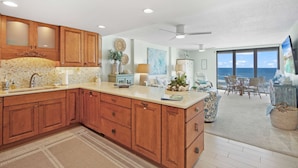 A spacious kitchen with wooden cabinets, a large island, and a view of the ocean through the dining area.