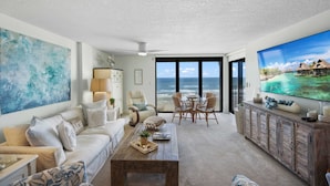 A spacious living room with a large TV, comfortable seating, and a view of the ocean.