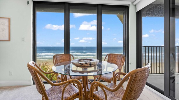 A balcony with a glass table and wicker chairs, overlooking the ocean.