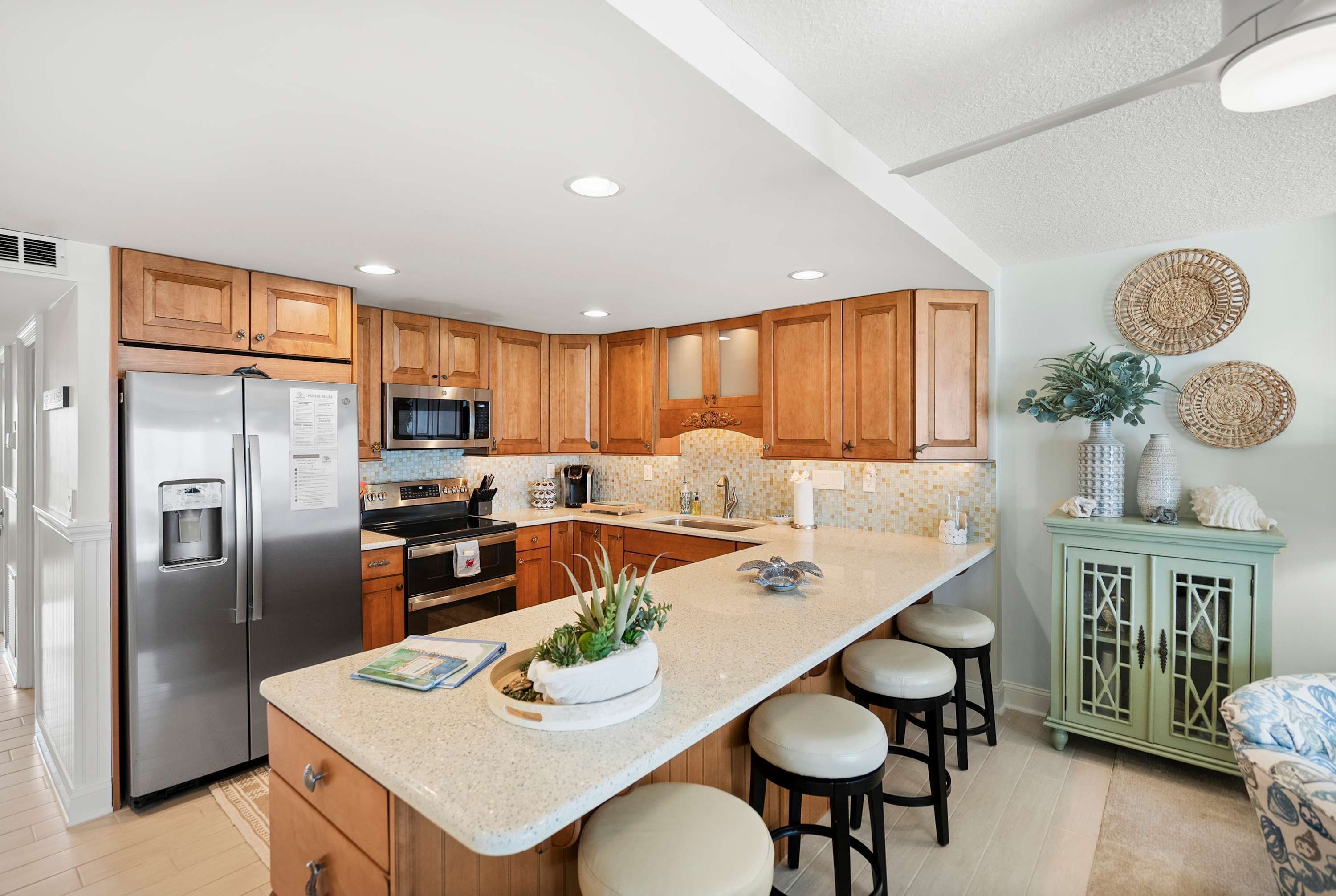 A modern kitchen with wooden cabinets, stainless steel appliances, a central island with stools, and decorative wall art.
