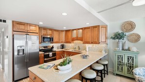 A modern kitchen with wooden cabinets, stainless steel appliances, a central island with stools, and decorative wall art.